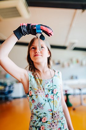 Ein Mädchen hält an einer Hand mit einem Handschuh einen Magneten und einen Löffel