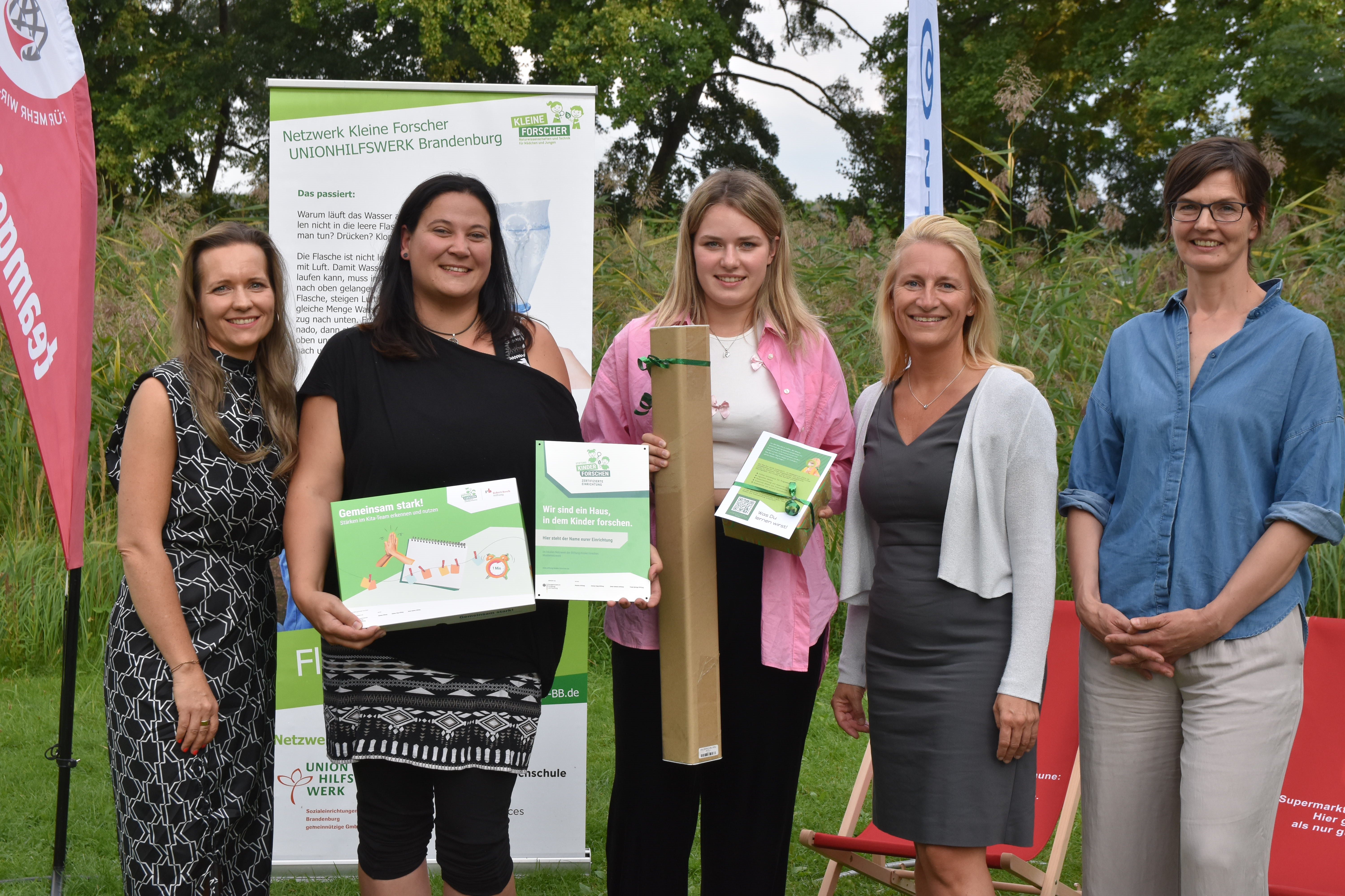 Fünf Frauen mit PLaketten vor Aufstellern.