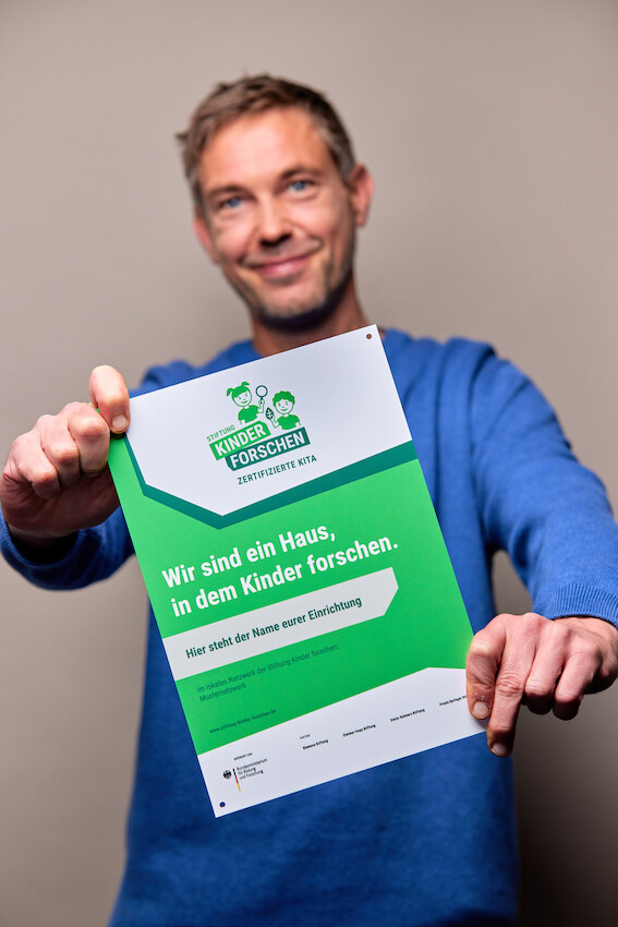 Mitarbeiter der Stiftung hält die große Zertifizierungs-Plakette in die Kamera