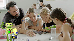 Ein Lehrer sitzt neben drei Grundschülerinnen, die ein Tablet bedienen.