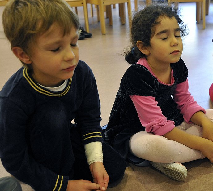Zwei Kinder sitzen auf dem Boden mit geschlossenen Augen.