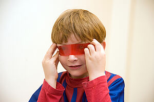 Ein Junge hält sich eine rote Farbfolie vor die Augen.