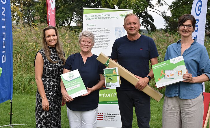 Vier Menschen vor den Aufstellern von Kinder forschen Unionshilfswerk Brandenburg.