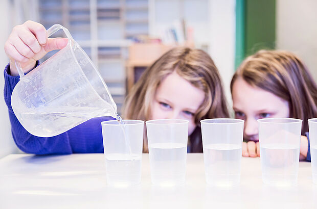 Zwei Mädchen gießen Wasser aus einem Messbecher in Gläser