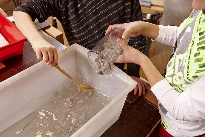 Kind füllt Ppaierbrei in Box mit Wasser