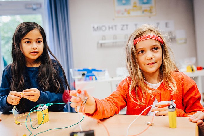 Zwei Mädchen verbinden eine Leuchte mithilfe von Kabeln mit Batterien.