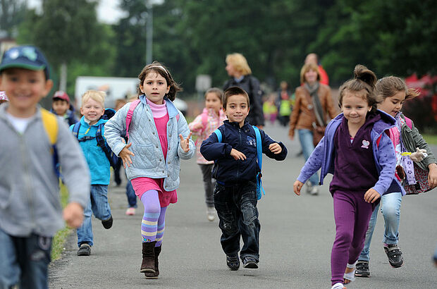 Mehrere Kinder mit Rucksäcken rennen einen Weg entlang