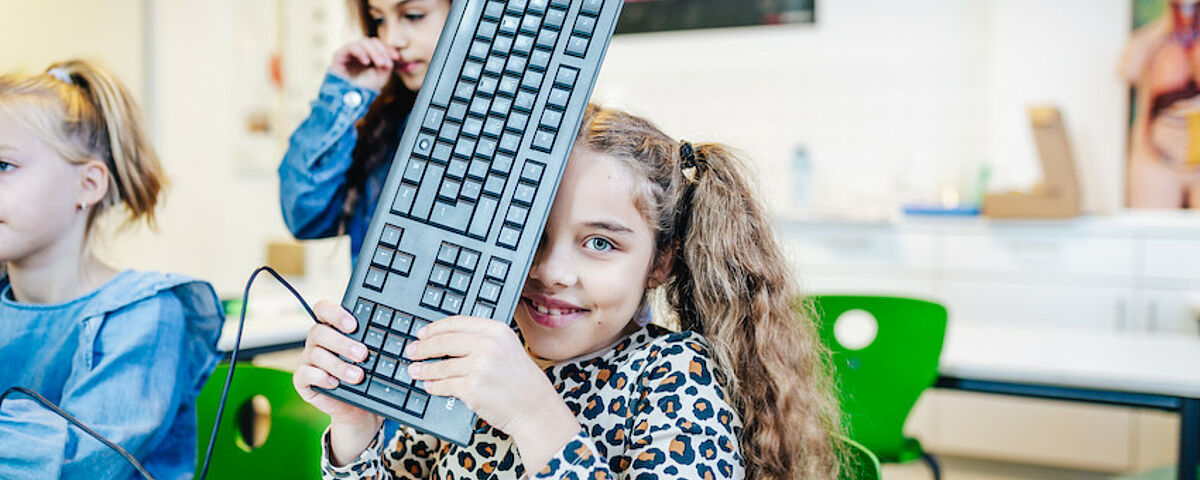 Ein Mädchen hält eine Tastatur hoch und lächelt in die Kamera
