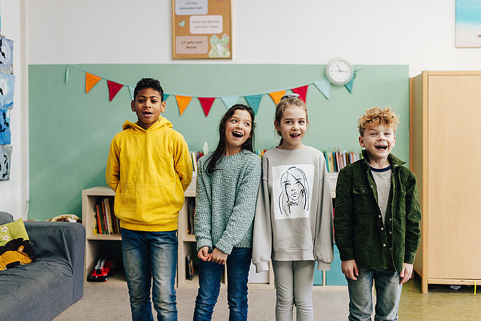 Vier Kinder stehen nebeneinander im Klassenzimmer und singen