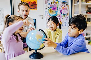 Kinder und ein Lehrer erkunden einen Globus.