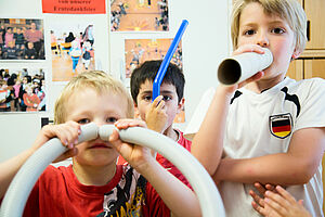 Drei Kinder experimentieren mit verschiedenen Rohren und Schläuchen.