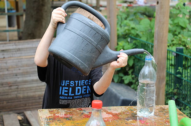 Kind schenkt Wasser aus Gießkanne in Plastikflaschen