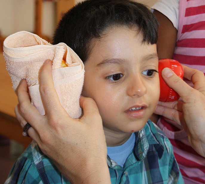 Junge hält eine Eieruhr in ein Handtuch gewickelt an sein Ohr.