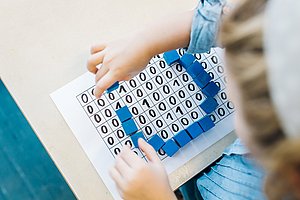 Kind legt blaue Bausteine auf ein Papier und entdeckt die Welt der Informatik