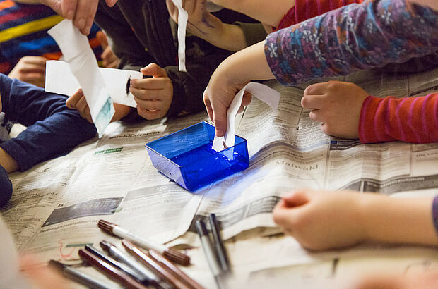 Kinder tunken Papier in eine blaue Schale mit einer Flüssigkeit darin