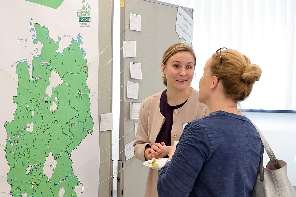 Zwei Frauen stehen vor einer grün gefärbten Deutschlandkarte und unterhalten sich.