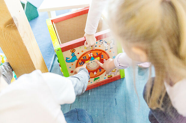 Kinder zeigen auf ein Ziffernblatt einer Spieluhr