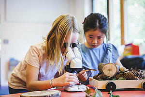 Ein Mädchen untersucht mit einem klassischen Mikroskop eine Beere.