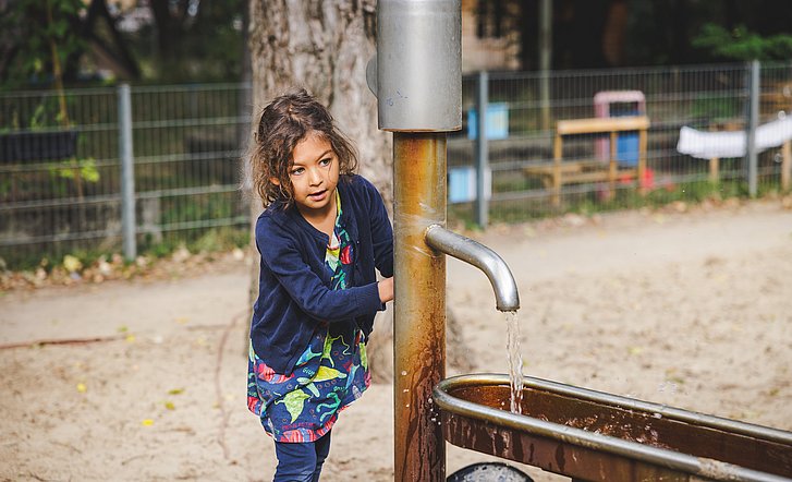 Kind pumpt Wasser aus einer Wasserpumpe im Kita-Garten