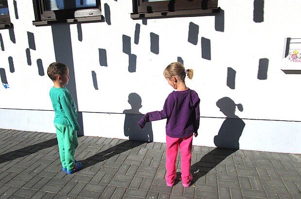 Die Schatten zweier Kinder zeichnen sich auf einer Hauswand ab.