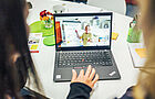 Zwei Frauen sitzen vor einem aufgeklappten Laptop und schauen sich eine Online-Fortbildung an.