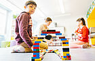 Kinder spielen mit einer Brücke aus Legosteinen.
