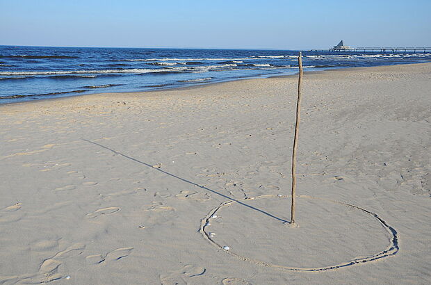 Ein Stock ist am Strand in den Sand gesteckt und dient so als Sonnenuhr.