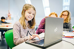 Mädchen sitz am Laptop und eine Lehrerin im Hintergrund