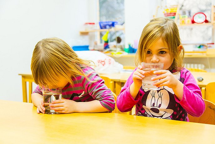 Zwei Kita-Mädchen riechen an Wassergläsern