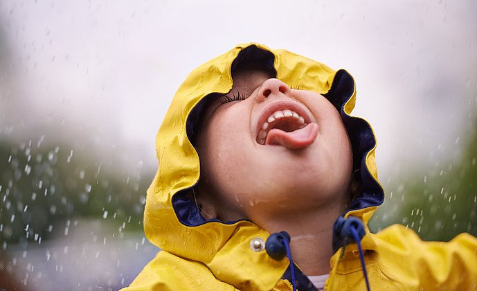 Junge in gelber Regenjacke streckt seine Zunge dem Regen entgegen