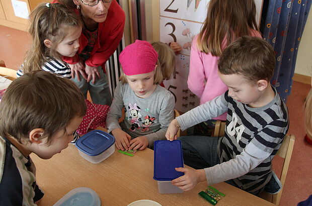 Kinder probieren Deckel auf runden und eckigen Dosen aus