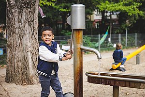 Kind pumpt Wasser mit einer Pumpe im Garten