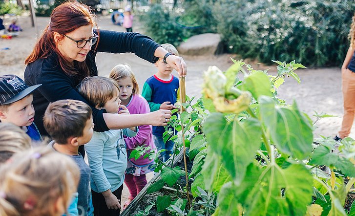 Pädagogische Fachkraft mit Kindern im Kita-Garten