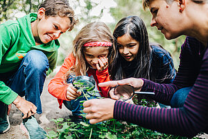 Kinder untersuchen gemeinsam mit einer Erzieherin Pflanzen unter einer Lupe